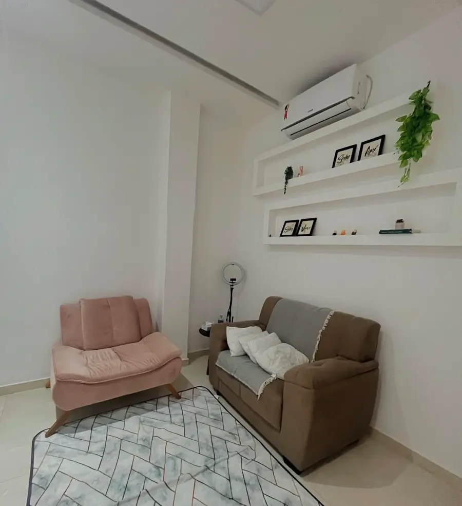 Sala de atendimento com poltrona rosa, sofá marrom e tapete