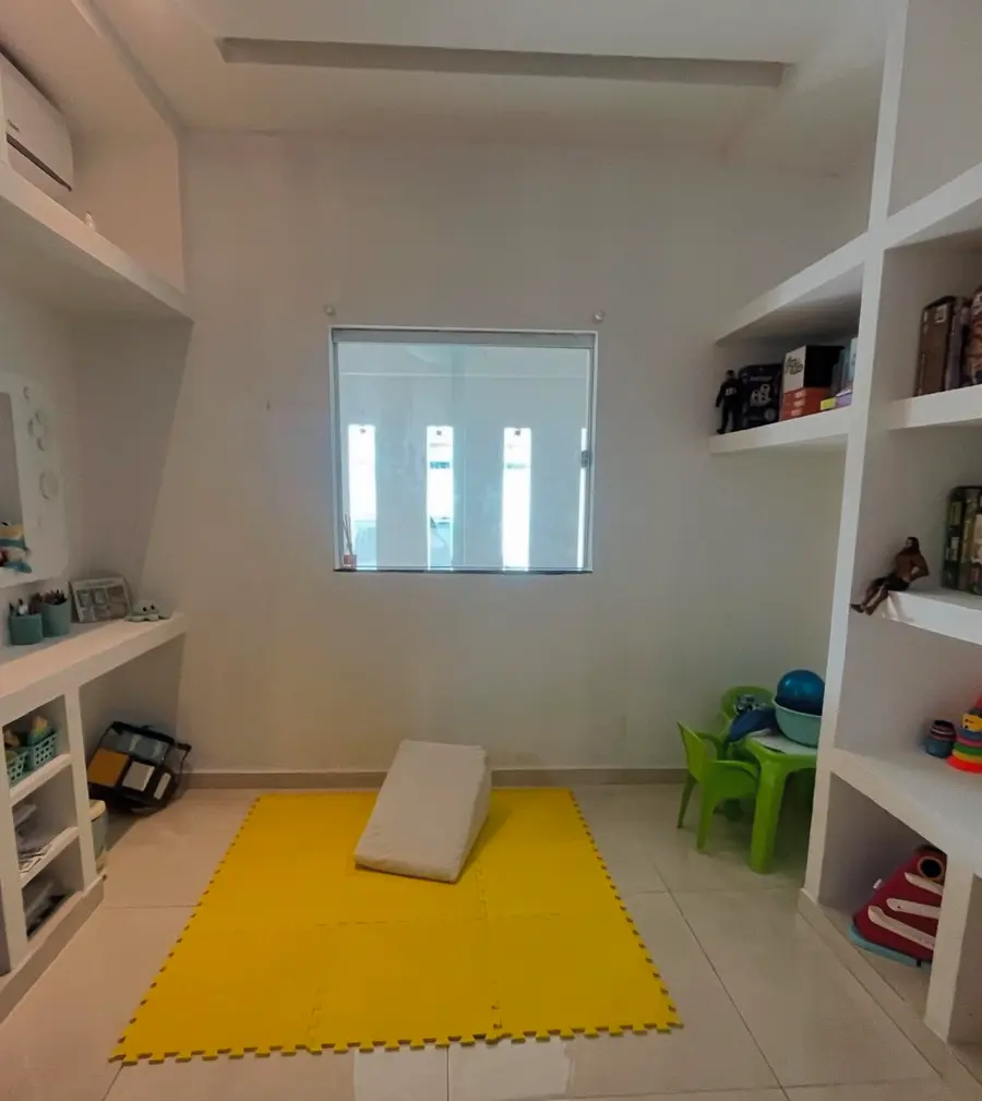 Sala de brincar com tapete amarelo, prateleiras brancas e banquinho verde