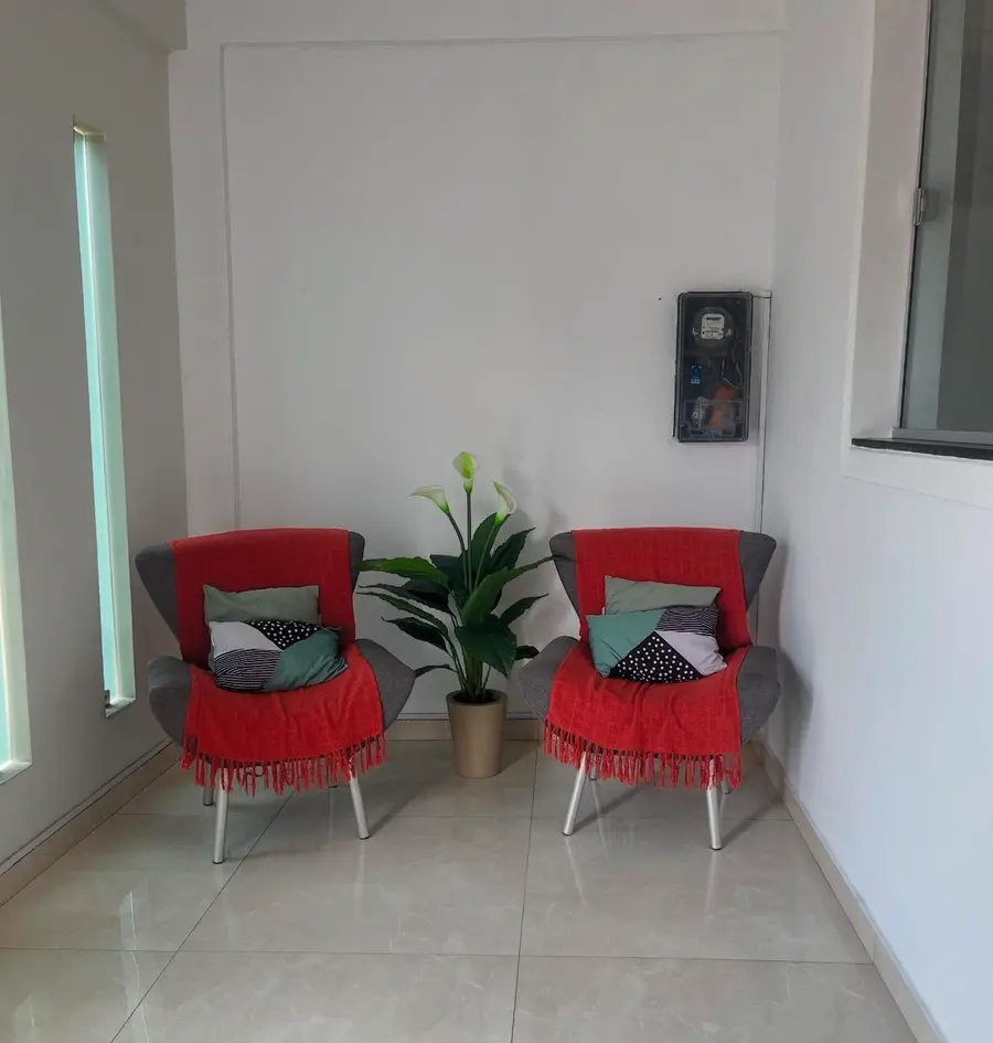 Sala de espera com duas poltronas vermelhas e uma planta